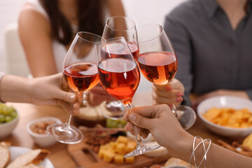 People clinking glasses with rose wine above wooden table indoors, closeup