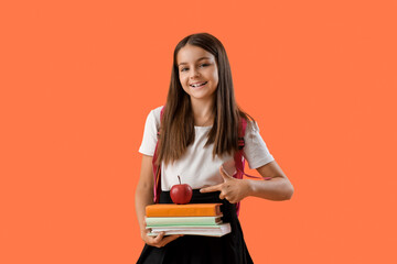 Wall Mural - Cute schoolgirl with books pointing at fresh apple on orange background