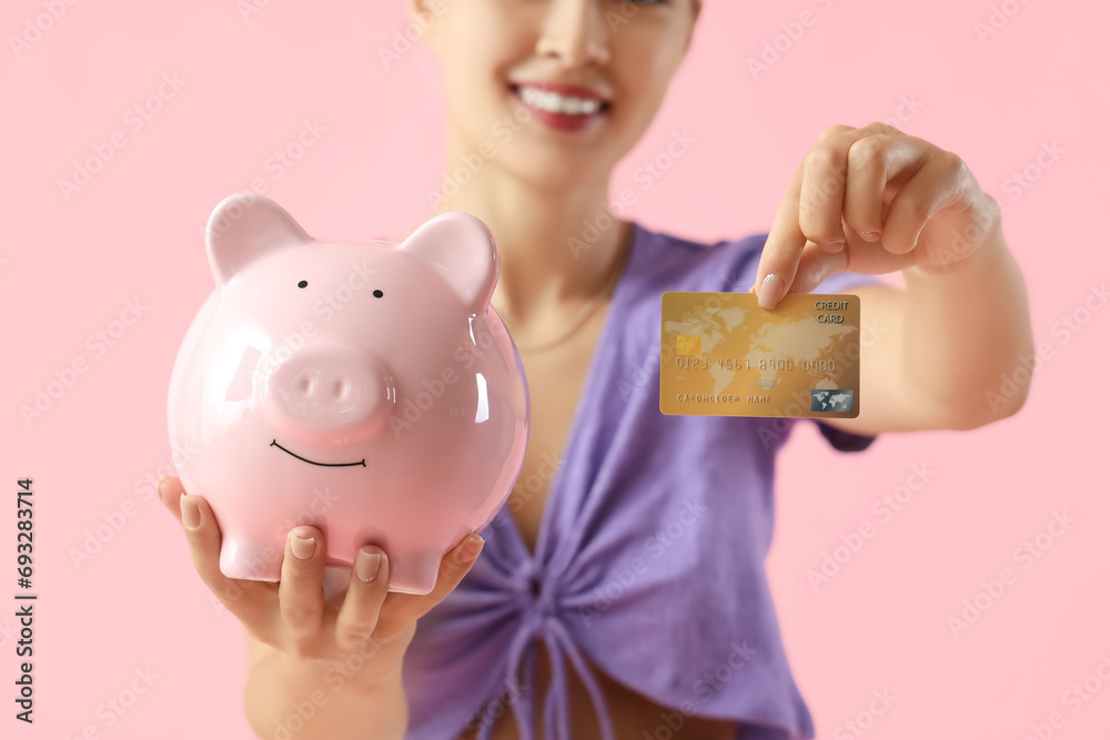 Young woman with credit card and piggy bank on pink background