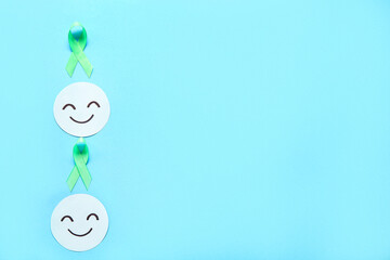 Wall Mural - Happy smile faces with green awareness ribbons on blue background. Mental Health Day