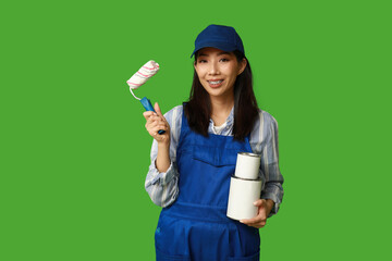 Female Asian painter with roller and paint cans on green background