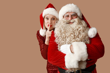 Sticker - Santa Claus and beautiful mature woman in Christmas hats showing silent gesture on brown background