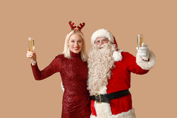 Poster - Santa Claus and beautiful mature woman in Christmas deer horns with glasses of champagne on brown background