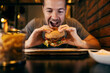 A hungry man biting a delicious hamburger at fast food restaurant.