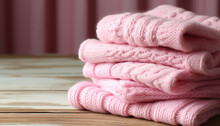 Stack Of Cozy Pink Knit Sweaters On A Wooden Surface Against A Blurred Background.