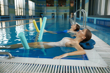 Wall Mural - Two women doing relaxing exercise with noodles after training in swimming pool