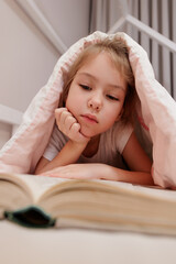 Wall Mural - portrait of bored little girl lying in bed and reading book