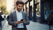 © venusvi - Smiling young businessman is using a smartphone while walking down the street,