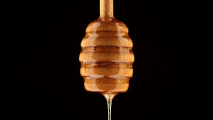 Poster - Thick honey dripping from a wooden honey spoon, isolated on black background