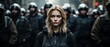 A determined young woman stands confidently in the foreground, with a phalanx of riot police blurred in the background.