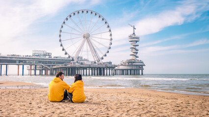 Wall Mural - couple on the beach of Scheveningen Netherlands during Spring, The Ferris Wheel at The Pier at Scheveningen in the Netherlands, Sunny spring day at the beach 