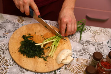 Crop anonymous female chef in uniform cutting fresh green parsley with knife on cutting board in kitchen