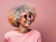 © ISVO - African american senior woman with afro hairstyle and sunglasses isolated on pink background. Close-up of an aged model smiling. Copy space for text