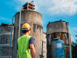 Asian man engineer controlling the quality of water places operating industrial water purification or filtration equipment old cement tanks for keeping water in water factory