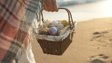 A Young Woman Walks Along The Beach At Sunset Carrying A Basket Of Easter Eggs. I'm Walking Towards The Sun, The Sea Waves Are Behind Me.