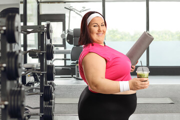 Sticker - Woman in sportswear holding a green smoothie and an exercise mat at a gym