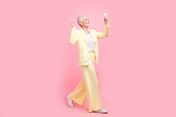 Sticker - Full body photo of smart person dressed yellow jacket walk in empty space talk on smartphone video call isolated on pink color background