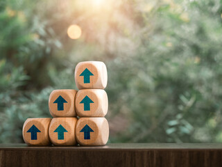 Poster - Rising up blue arrows on wooden cube blocks as a business graph or chart steps on table and green leaves background with copy space. Business growth, investment growing and success concepts.