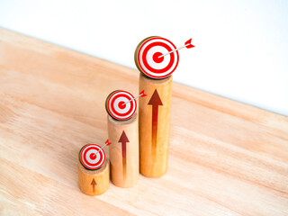 Poster - 3d Target icons and rise arrows on round wooden sticks as business graph steps on wood desk on white background. Business growth graph process, goal, success, and economic improvement concepts.