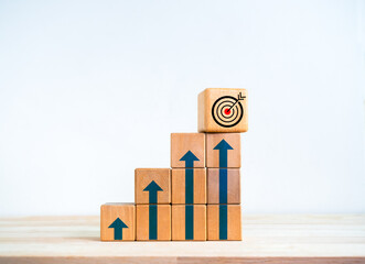 Poster - Target icon on wooden cube on top of wood blocks bar graph chart steps with blue rising arrows symbol on desk, white background. Investment, income, revenue, profit goal, business growth concepts.