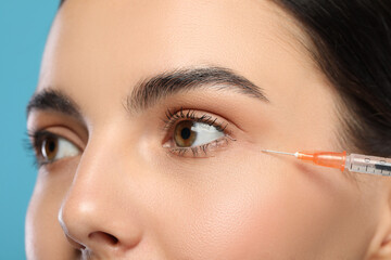 Wall Mural - Young woman getting facial injection on light blue background, closeup. Cosmetic surgery