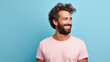 Happy, bearded man wearing a pink t-shirt, smiling and looking away to the side against a blue background