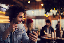 Smiling young man using smartphone in cafe