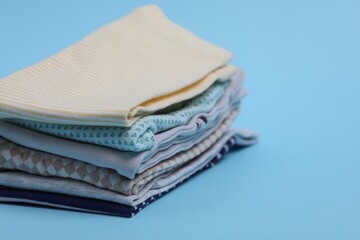 Wall Mural - Stack of clean baby clothes on light blue background, closeup. Space for text