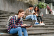 © M+Isolation+Photo - Happy diverse university students sitting on steps, using laptops and tablets, enjoying conversation. Student exchange and study abroad program, Asian man, african american woman and caucasian people.