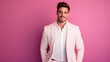 © Tattoo_SP - Image of a handsome young man wearing a white groom's suit, standing and smiling on a pink background.