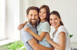© Studio Romantic - Close up portrait of a young happy family of three standing at home with their child girl looking at camera and smiling. Joyful parents hugging their daughter. Love, care and happy family concept.