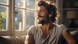 Fototapeta  - Joyful man with tattoos sitting by the window, sun streaming in, a moment of happiness and contentment captured in a cozy, sunlit room.