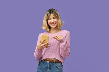Happy pretty gen z blonde young woman model holding smartphone looking at camera pointing on cell, smiling girl using mobile apps on cell phone standing isolated on purple background with cellphone.