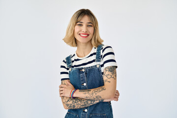 Happy pretty gen z blonde young woman, cute girl with short blond hair tattoos wearing striped t-shirt denim dress rainbow bracelet looking at camera standing isolated on white background. Portrait.