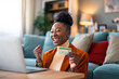 Enthusiastic charming black woman feeling excited using laptop and holding credit card satisfied with online payment possibilities, rejoicing approved loan.