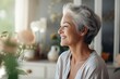 Beautiful elderly elegant gray-haired woman smiles, looks out the window or mirror. Background of room interior with flowers. Beautiful old age, chic well-groomed grandmother, anti-aging cosmetology