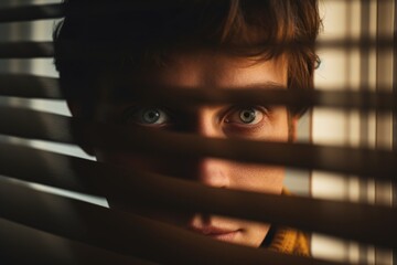 Poster - A young man is seen peering out of a window with blinds. This image can be used to depict curiosity, solitude, or a moment of contemplation. It is suitable for various themes and concepts
