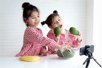 Two happy sister girls record social media channel blogger vlog on digital smartphone cam. Little blogger influencer talking about fruits healthy food diet, streaming online podcast on mobile phone.