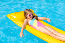 Cute Little Girl Lying On Inflatable Mattress In Swimming Pool With Blue Water On Warm Summer Day On Tropical Vacations. Summertime Activities Concept. Cute Little Girl Sunbathing On Air Mattress