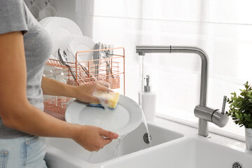 Wall Mural - Woman washing plate at sink in kitchen, closeup