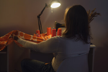 Senior woman sitting on a chair at home in her living room and working on her sewing machine