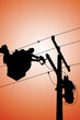 The silhouette of Electrical power line technicians perform maintenance on power lines by using a truck-mounted bucket.