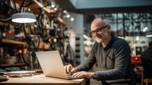Senior Man Working On Laptop In Bicycle Shop