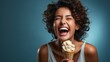 Joyful woman with curly hair laughing and enjoying a cone of vanilla ice cream, capturing a moment of happiness and indulgence against a serene blue background.