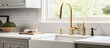 © AkuAku - A detailed photo of a kitchen sink featuring a farmhouse sink, gold faucet, grey cabinets, white marble countertop, and circular tiled backsplash.