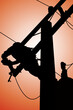 The silhouette of power lineman climbing on an electric pole with a transformer installed. And replacing the damaged hotline clamp, bail clamp, dropout fuse cutout that causes a power outage.