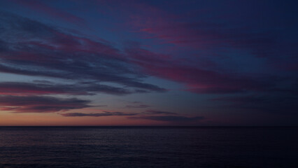 Beautiful sunset with purple clouds and flying birds over the sea