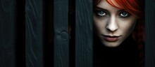 Red-haired enchantress woman in black carnival costume peeks out from behind a fence or wooden wall on All Saints' Day.