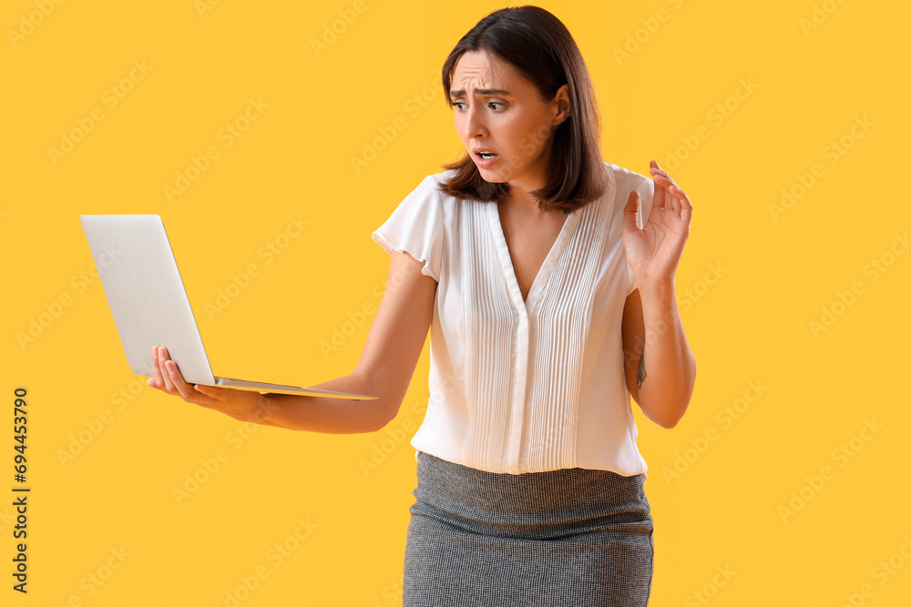 Young afraid woman with laptop on yellow background