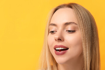 Wall Mural - Young woman taking vitamin A pill on yellow background, closeup